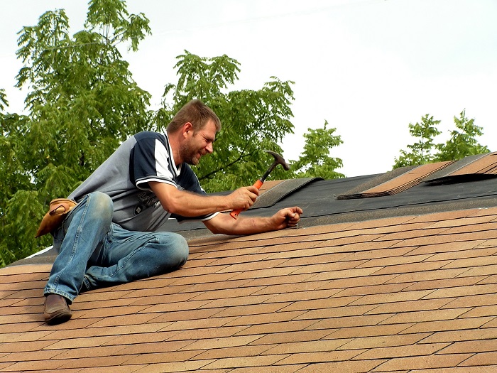 Man hammering shingles on an unfinished roof.
